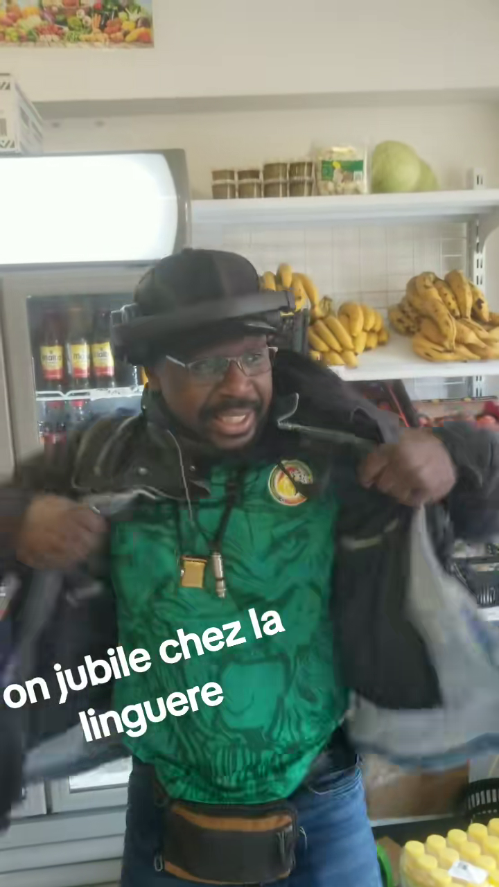 Un homme en maillot vert du Sénégal, chapeau et lunettes, danse joyeusement au milieu des rayons de l'épicerie africaine La Linguere, devant des régimes de bananes et des rayons de produits.