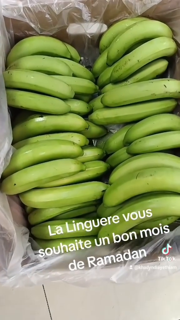 Caisse remplie de bananes vertes fraîches posée sur le sol carrelé de l'épicerie africaine La Linguere à Toulouse.