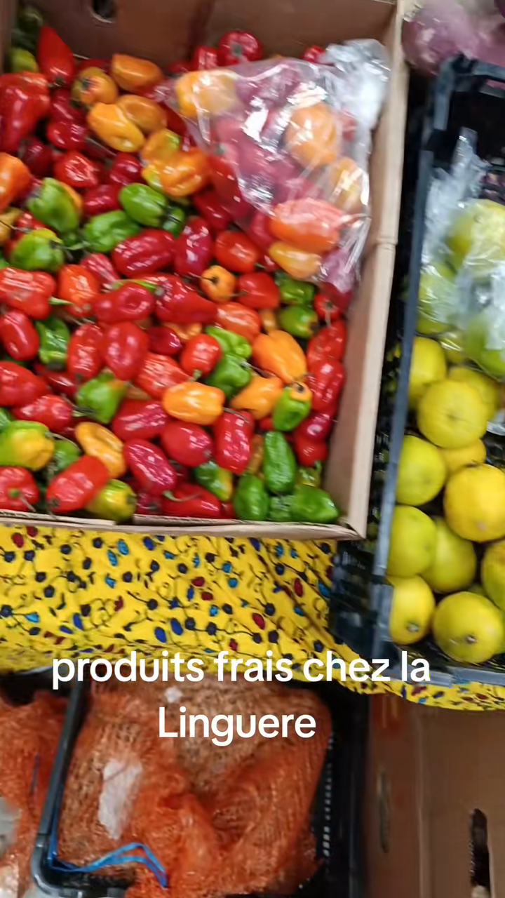 Cageot de piments rouges, verts et orange mélangés à des citrons verts sur un étal de produits frais de l'épicerie La Linguere.